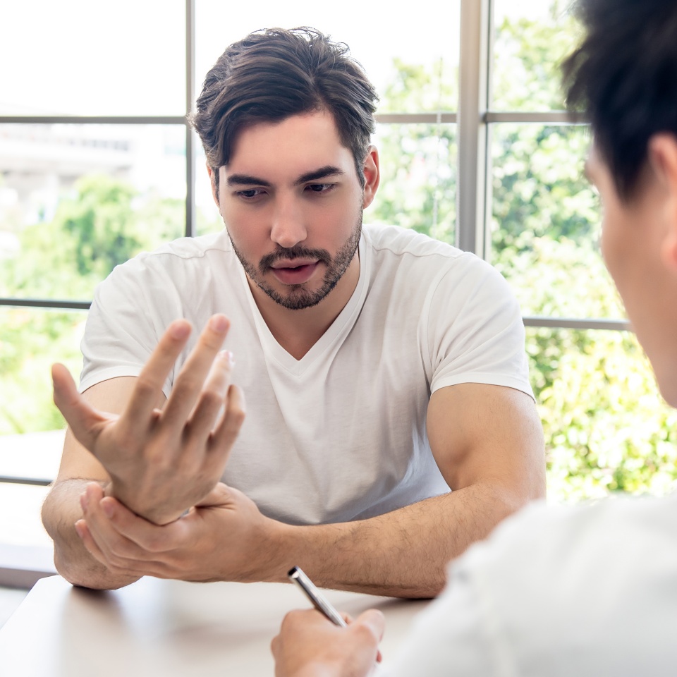 Young handsome athlete male patient consulting with doctor for wrist pain in clinic, sports medicine concept