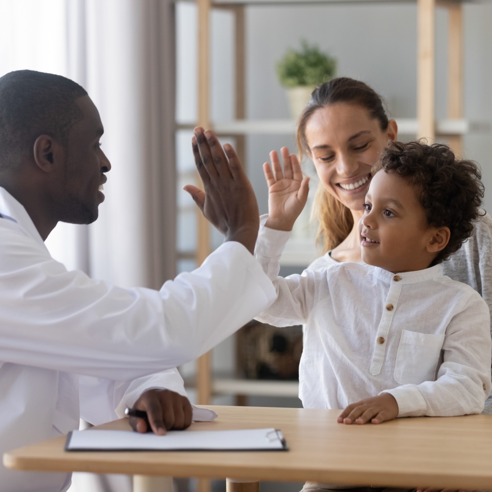 Happy cute multiracial child boy give high five to african man pediatrician welcome little patient and mom at consultation trusting kid with doctor celebrate good medical health care treatment result