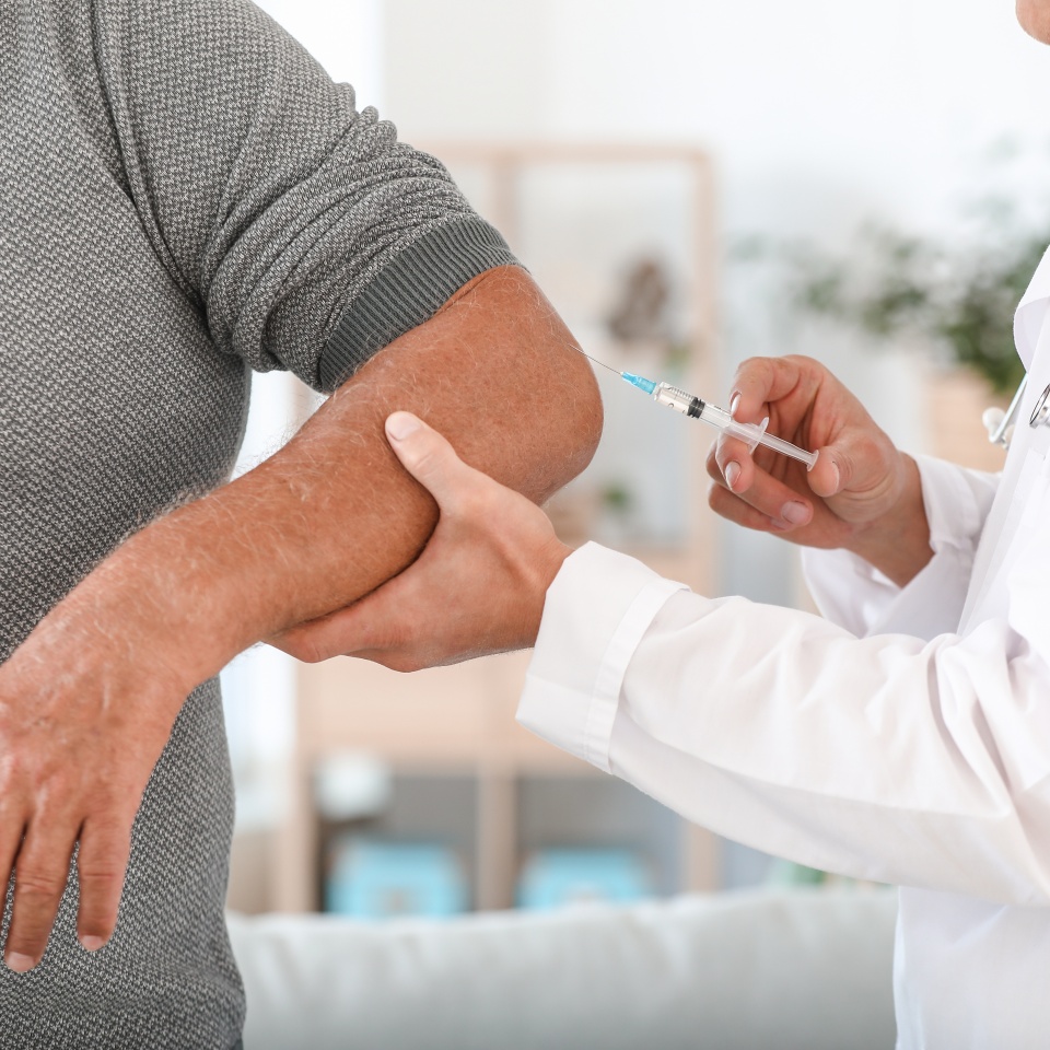 Doctor giving mature man with joint pain injection at home, closeup
