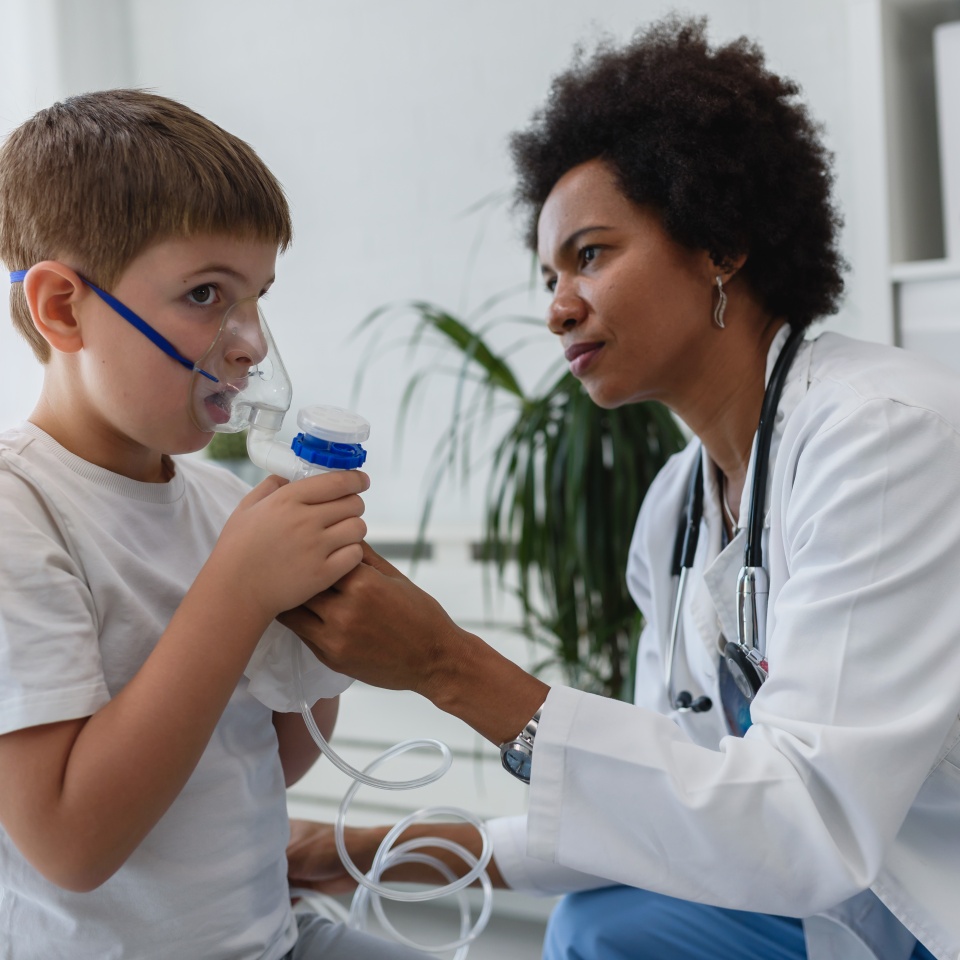 Woman African American doctor general practitioner helping child to put nebulizer inhaler face mask. Asthma treatment for children.
