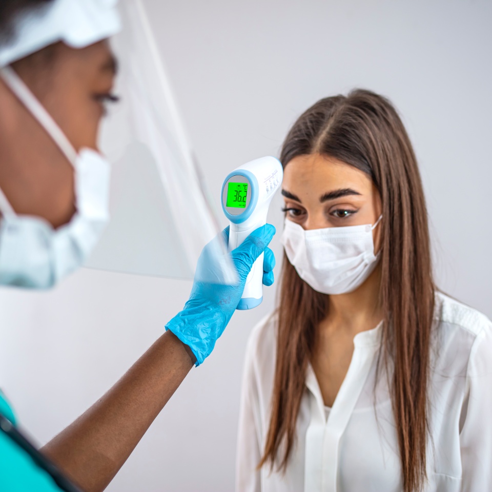 Measuring temperature with infrared thermometer of a young woman in face mask at a checkpoint during an epidemic outdoors. Concept of prevention the spread of the virus