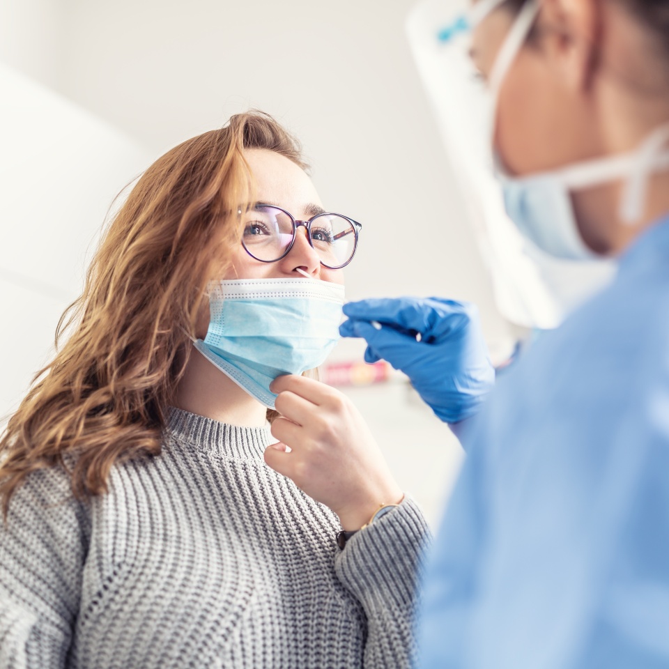 Smiling girl puts face mask off her nose so that a healthcare worker can take a sample for Covid-19 testing.