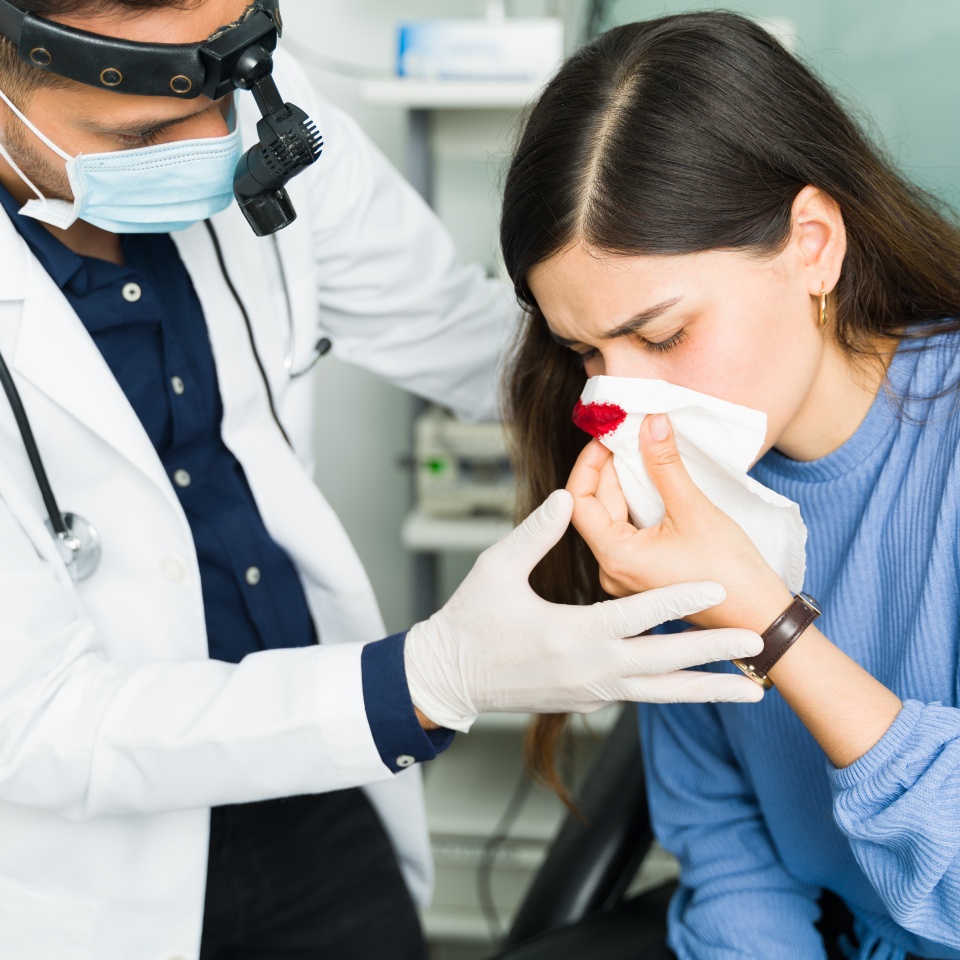 Professional otolaryngologist trying to stop a nasal hemorrhage of a female patient. Latin woman suffering from a nosebleed at the doctor