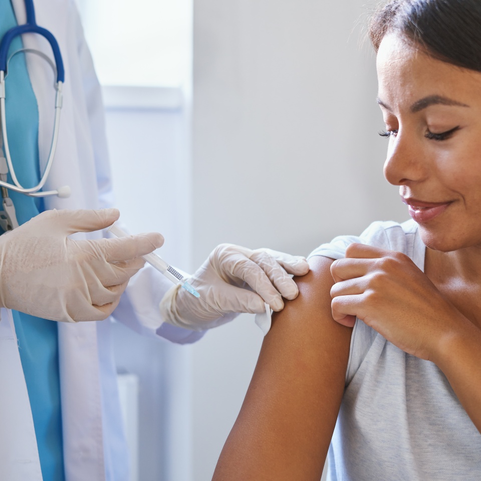 Young afro american woman receiving injection of coronavirus vaccine during appointment in clinic, doctor in uniform with syringe vaccinating female patient in hospital. Immunisation and vaccination