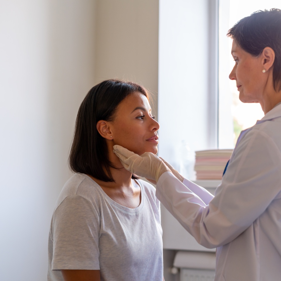 Laryngitis treatment. Middle-aged woman general practitioner examining throat of young afro american female patient visiting doctor in medical clinic. Diadnose consulting