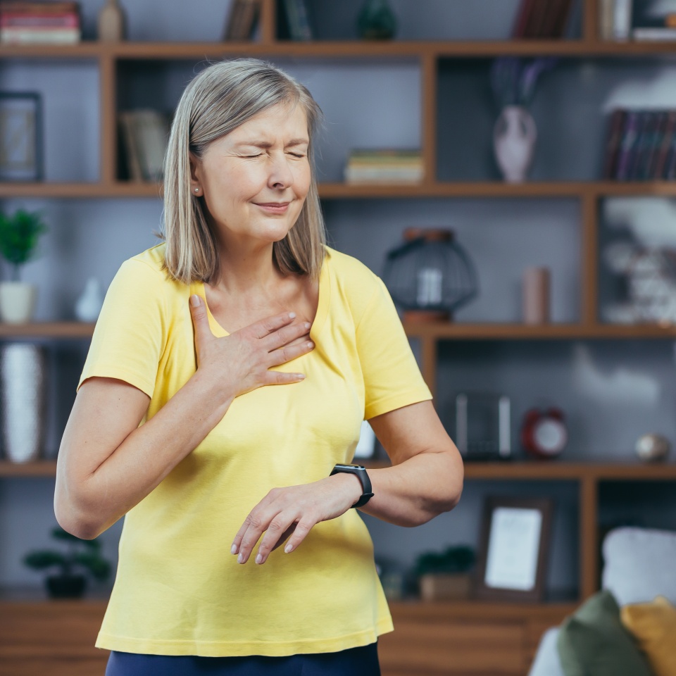 Older woman at home doing fitness has severe shortness of breath and chest pain, compares bullets on fitness bracelets
