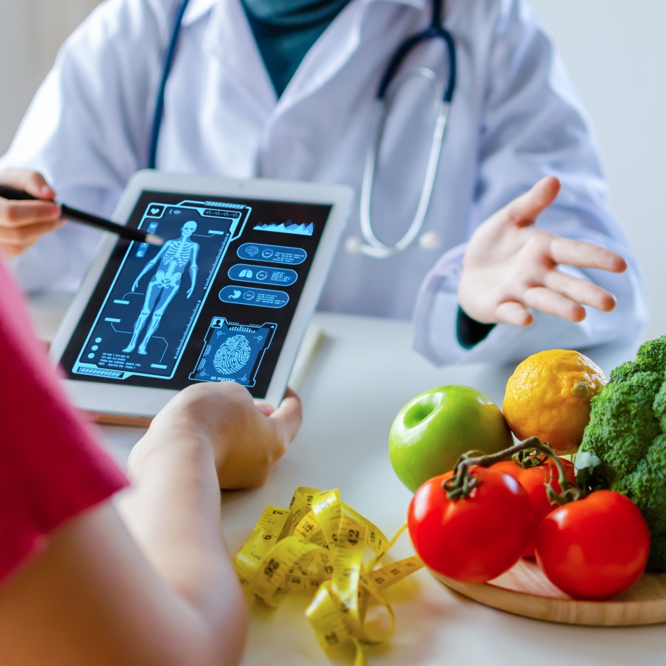 nutritionist female doctor using digital mobile tablet with virtual graphic icon diagram and vegetable and fruit with patient on desk at office hospital, nutrition, food science, healthy food concept
