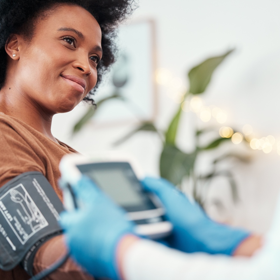 Black woman, healthcare and blood pressure machine in checkup with caregiver for monitoring pulse at home. Happy African American female patient or visit from medical nurse for health and wellness
