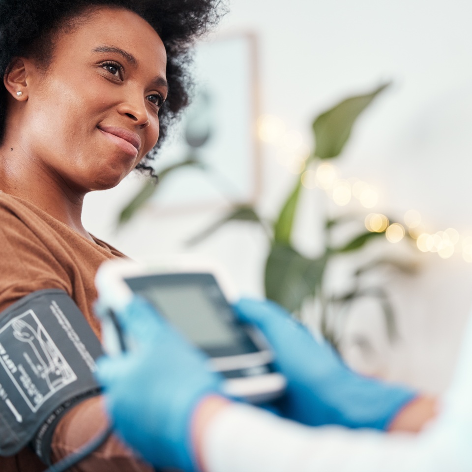 Black woman, healthcare and blood pressure machine in checkup with caregiver for monitoring pulse at home. Happy African American female patient or visit from medical nurse for health and wellness