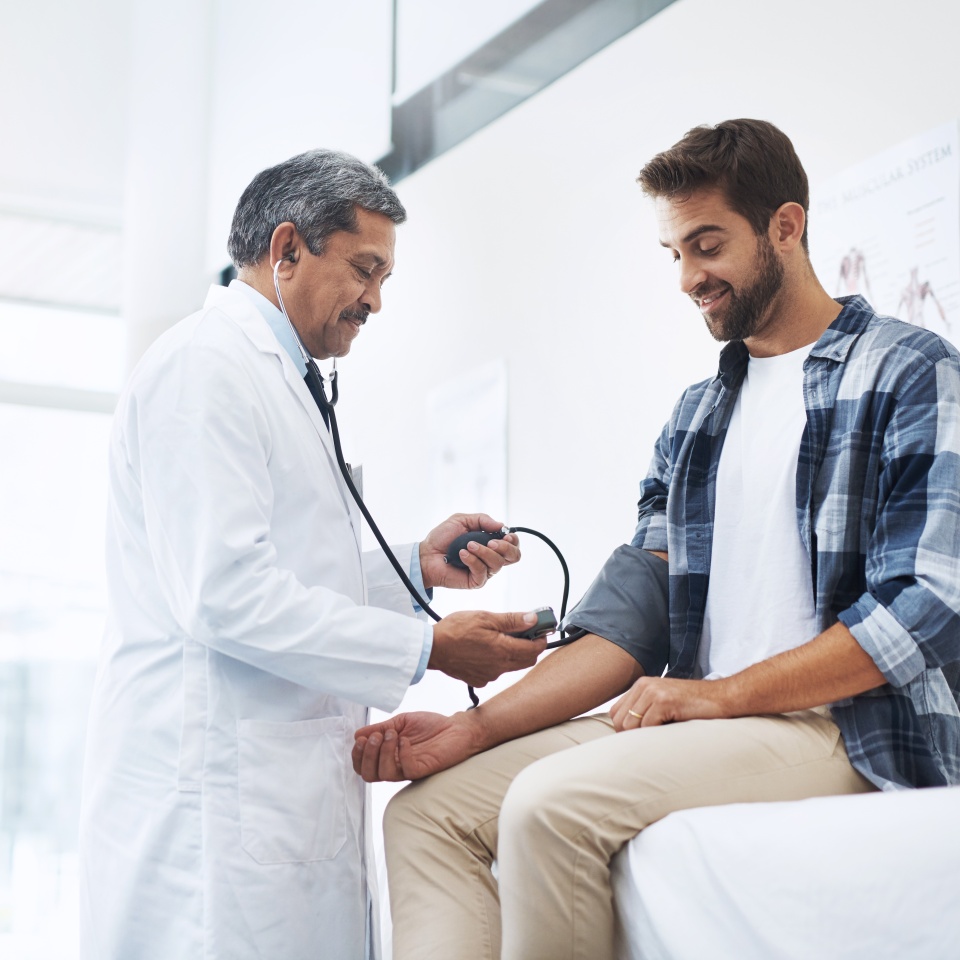 Healthcare, patient and doctor with blood pressure test, help and wellness checkup of person at hospital. Medicine, health care expert and Indian man in doctors office consulting medical professional