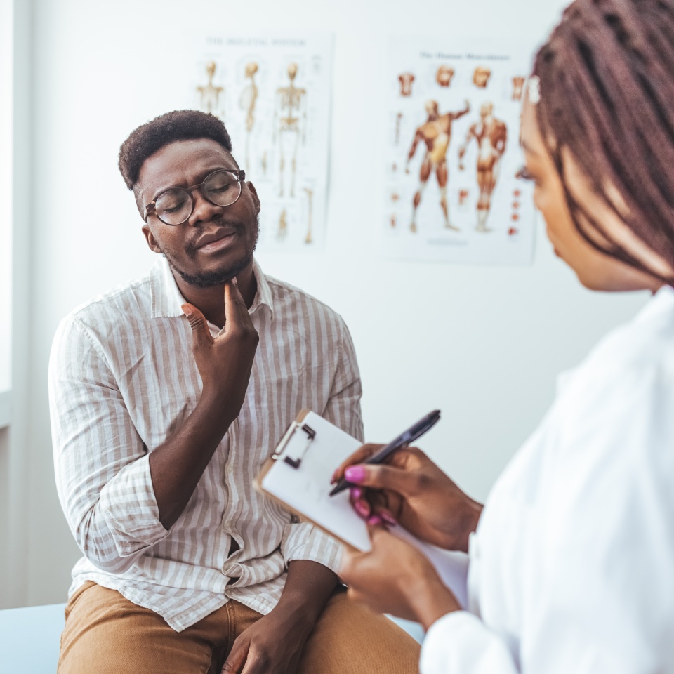Doctor listens to the patient's complaints while the patient points to the Throat. A doctor listens to a man patient describe throat pain. Young man have problem with sore throat or thyroid gland.