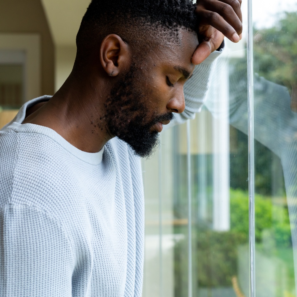 Thoughtful african american man leaning against window at home. Lifestyle, relaxation and domestic life, unaltered.