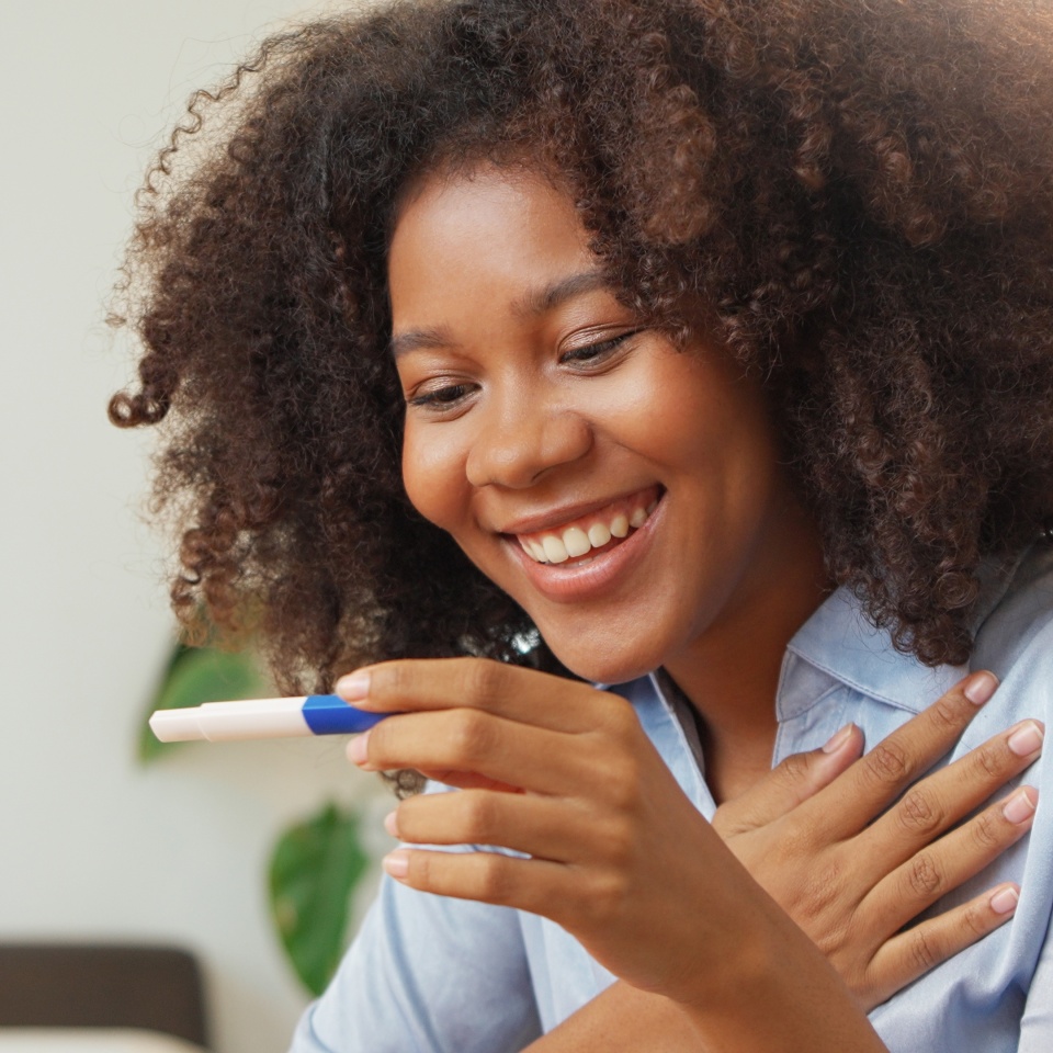 Excited Black African American woman in curly hair looking at pregnancy test. Positive results of a pregnancy test. Delighted, Surprise.