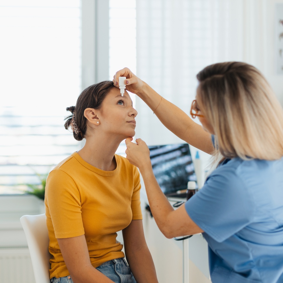 Pediatrician putting eye drops into girls eyes. The ophthalmologist treating an eye infection, allergy, or inflammation using prescribed eye drops.