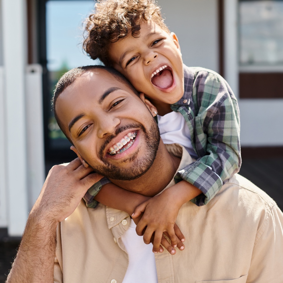 positive african american boy hugging excited father in braces on backyard of house, quality time