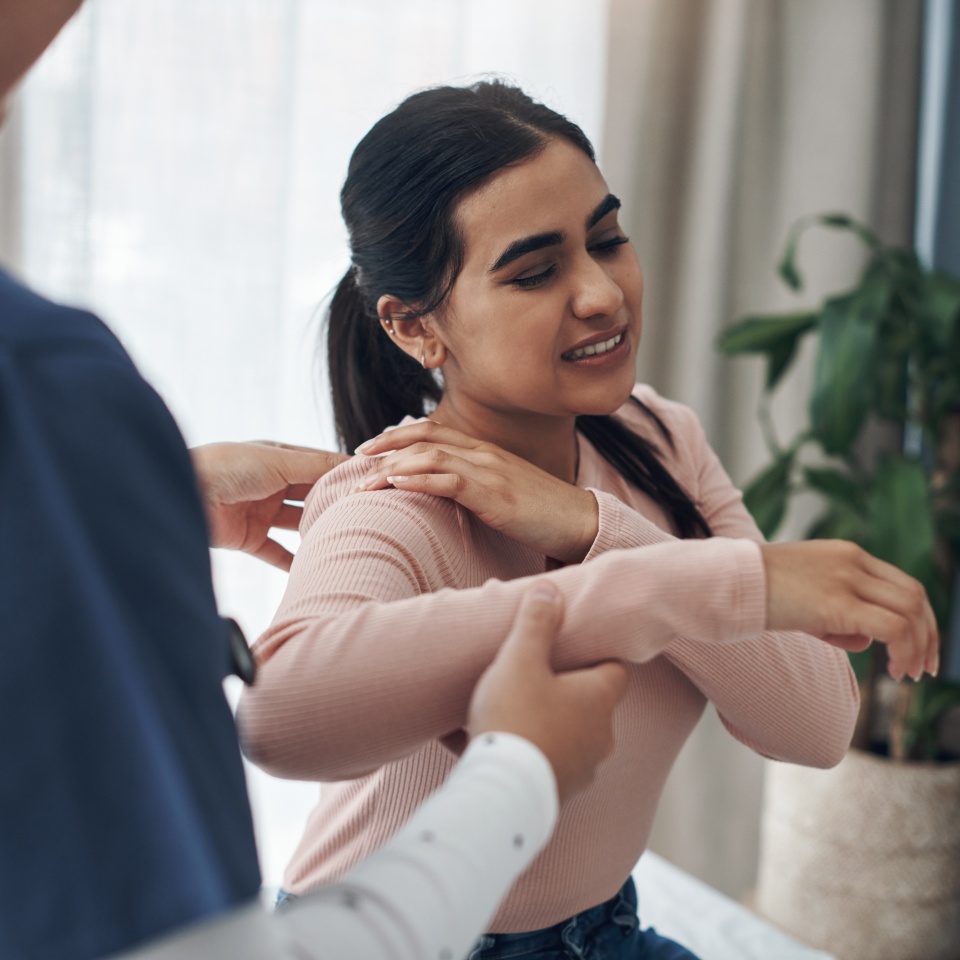 Woman, doctor and appointment with shoulder pain, medical and patient conversation for health care concern. Clinic, muscle tension and talking with medic employee, injury and professional help