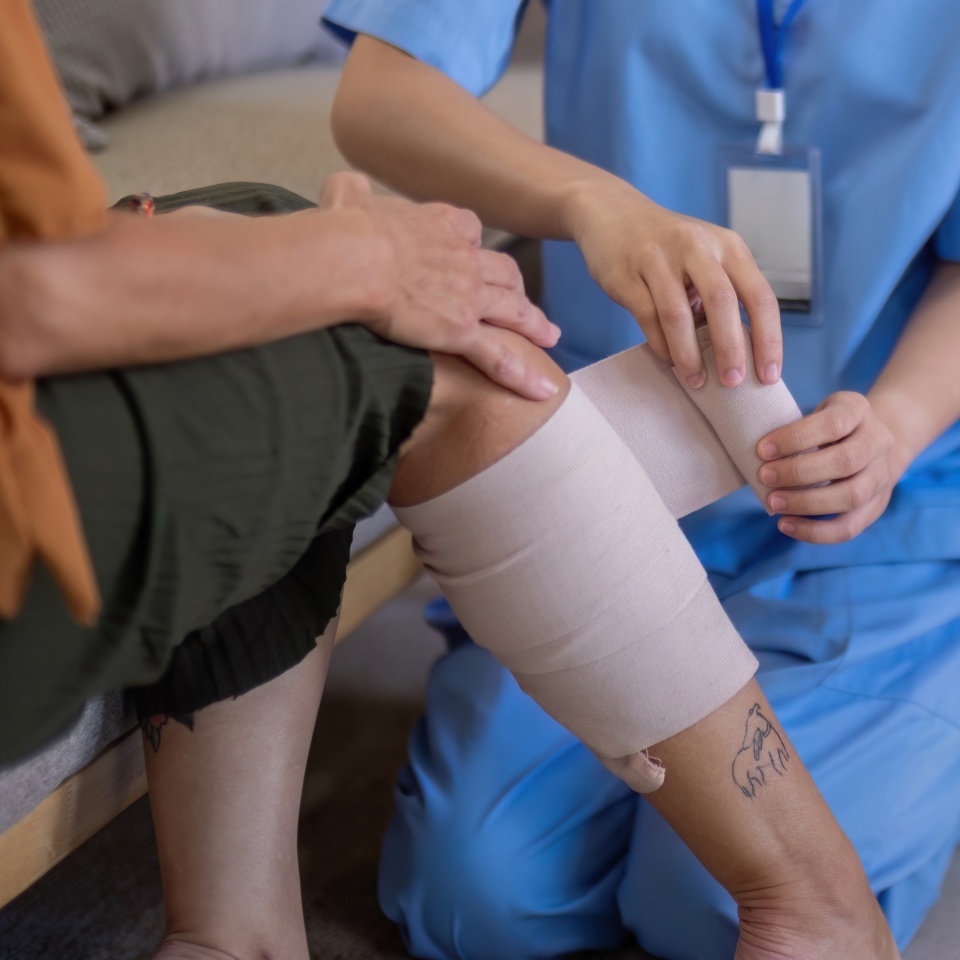 Close up of Asian caregiver bandaging elderly woman's leg at home. Concept of elderly care and wound management