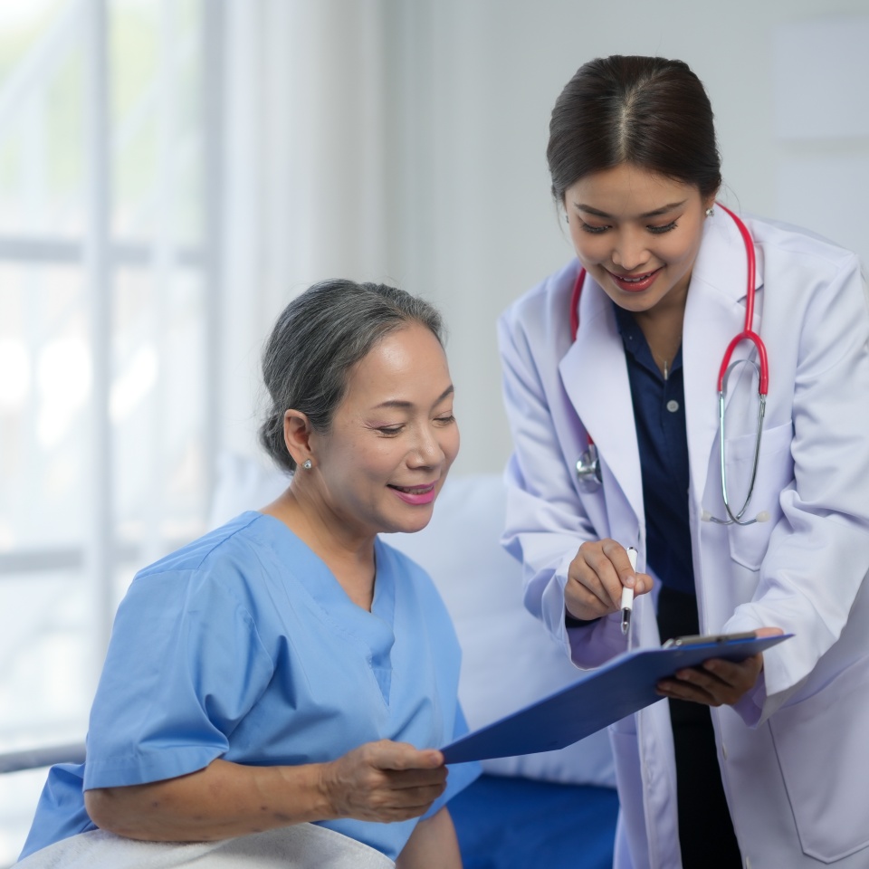 Doctor discussing medical report with elderly patient in hospital. Healthcare professional providing information to senior woman in hospital bed.