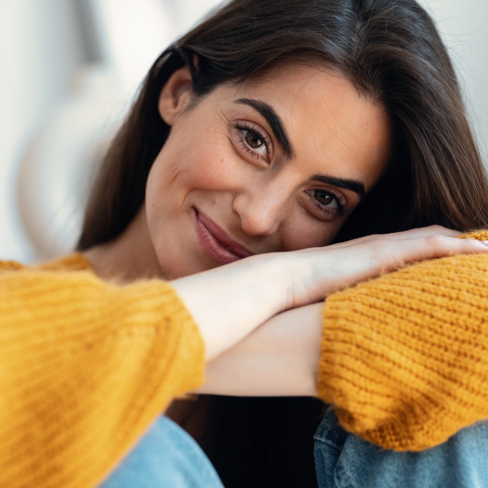 Portrait of scute young woman looking at camera while sitting on sofa at home.