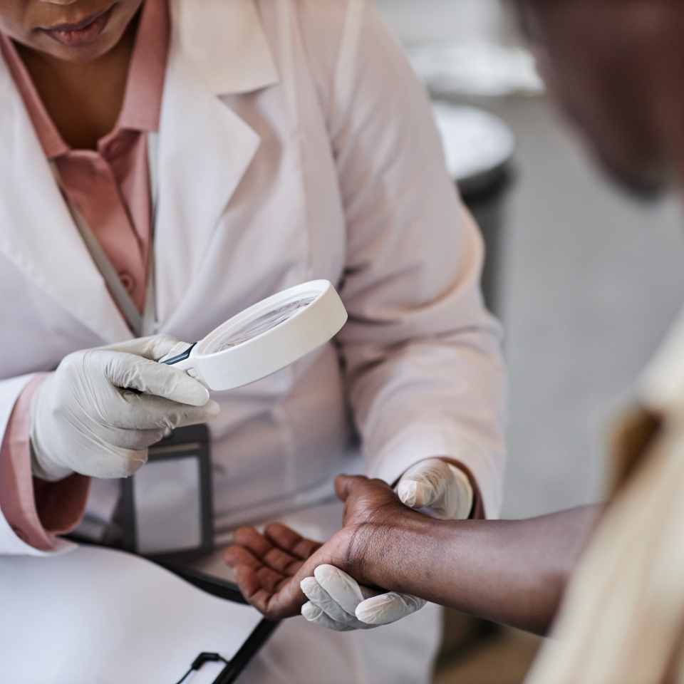 Close up of unrecognizable dermatologist using magnifying glass while examining patients arms during consultation in clinic
