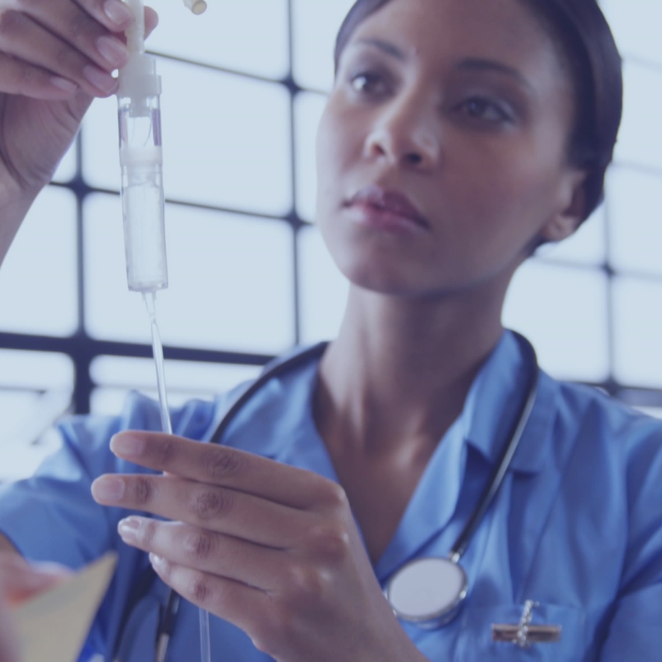Nurse in blue scrubs with stethoscope adjusting drop chamber and regulator on metal stand in clinic. Medical, healthcare, clinical, professional, patient care, equipment, bright