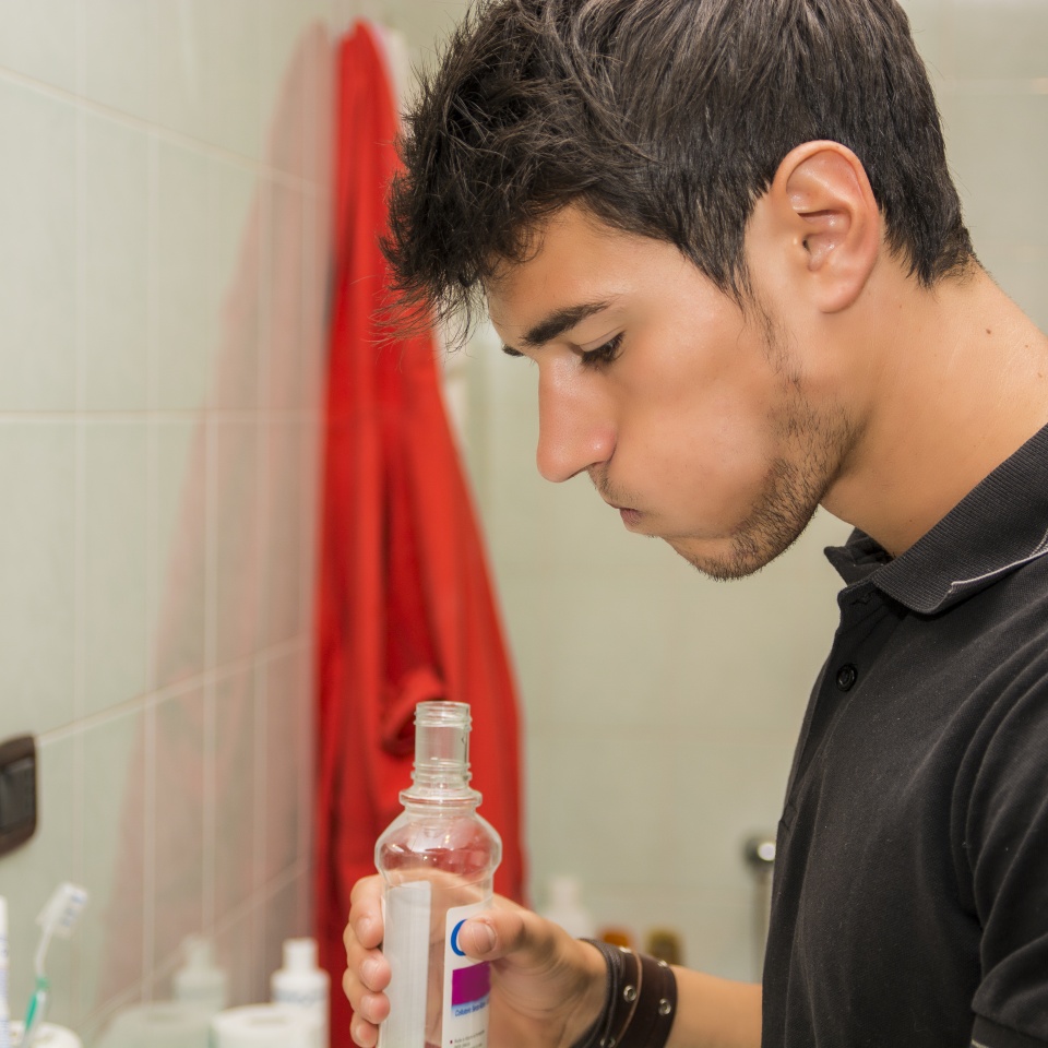 Head and Shoulders Close Up of Attractive Young Man with Dark Hair Rinsing with Mouth Wash in Bathroom as part of Morning Grooming Routine