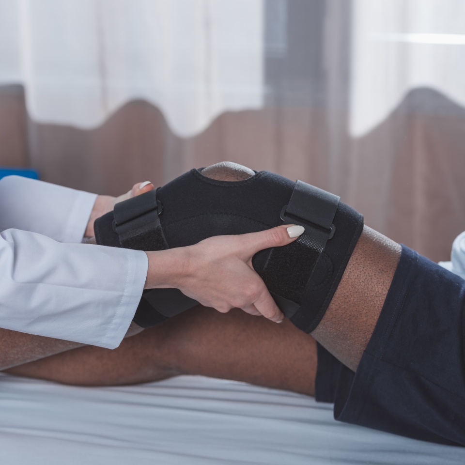 Cropped image of doctor putting on knee brace to african american patient