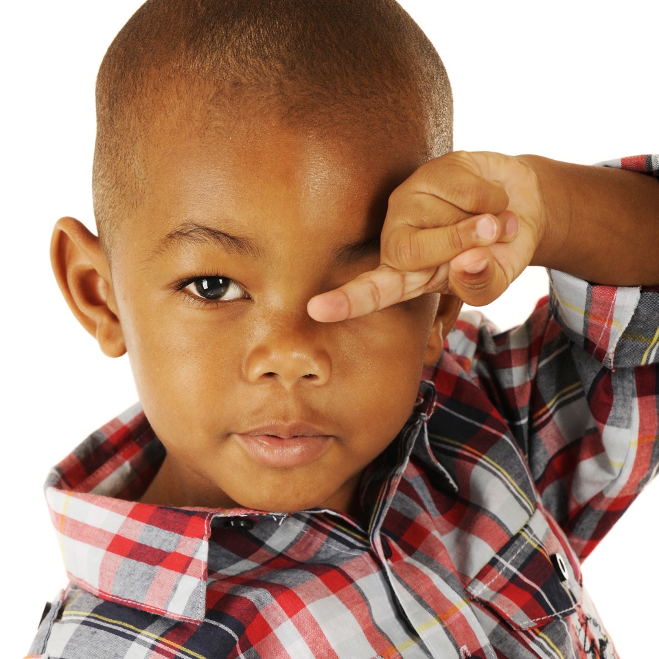 An adorable preschooler rubbing his eyes while pointing with his finger. On a white background.
