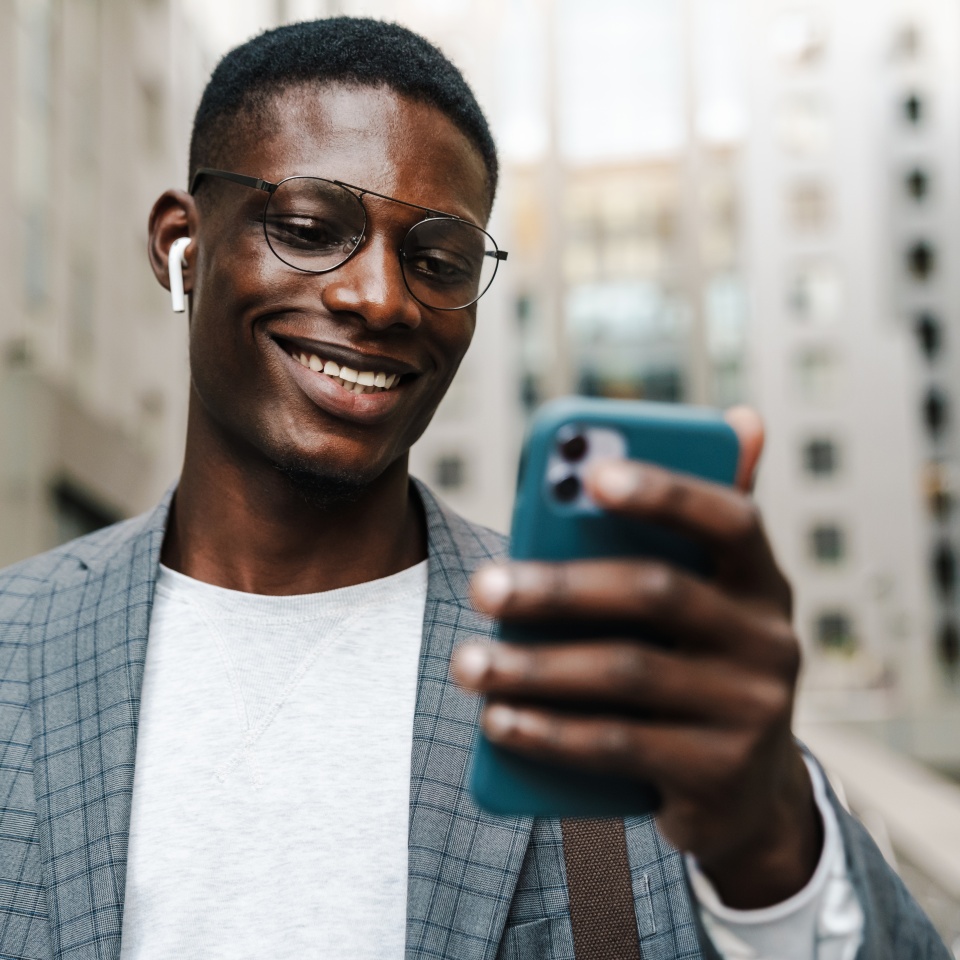 Happy african american man in earphones using mobile phone on city street