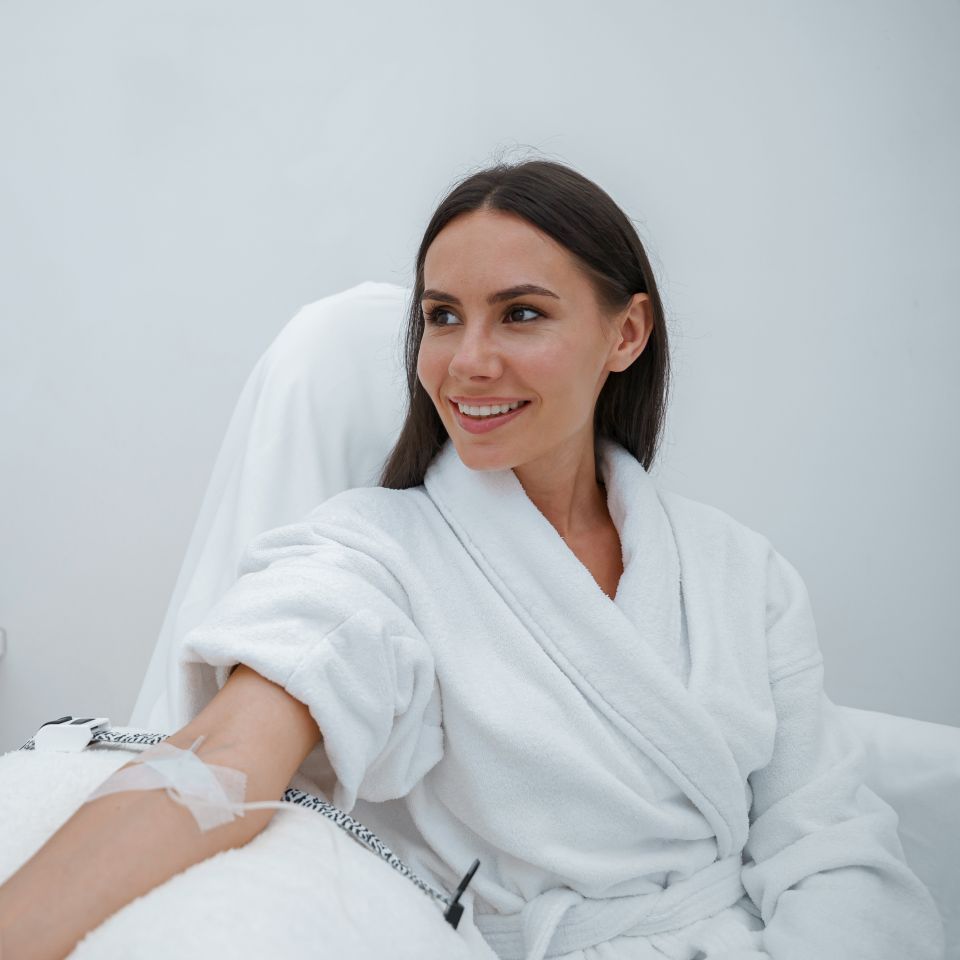 A beautiful woman with long dark hair wearing a white bathrobe getting Beatuy IV Drip.