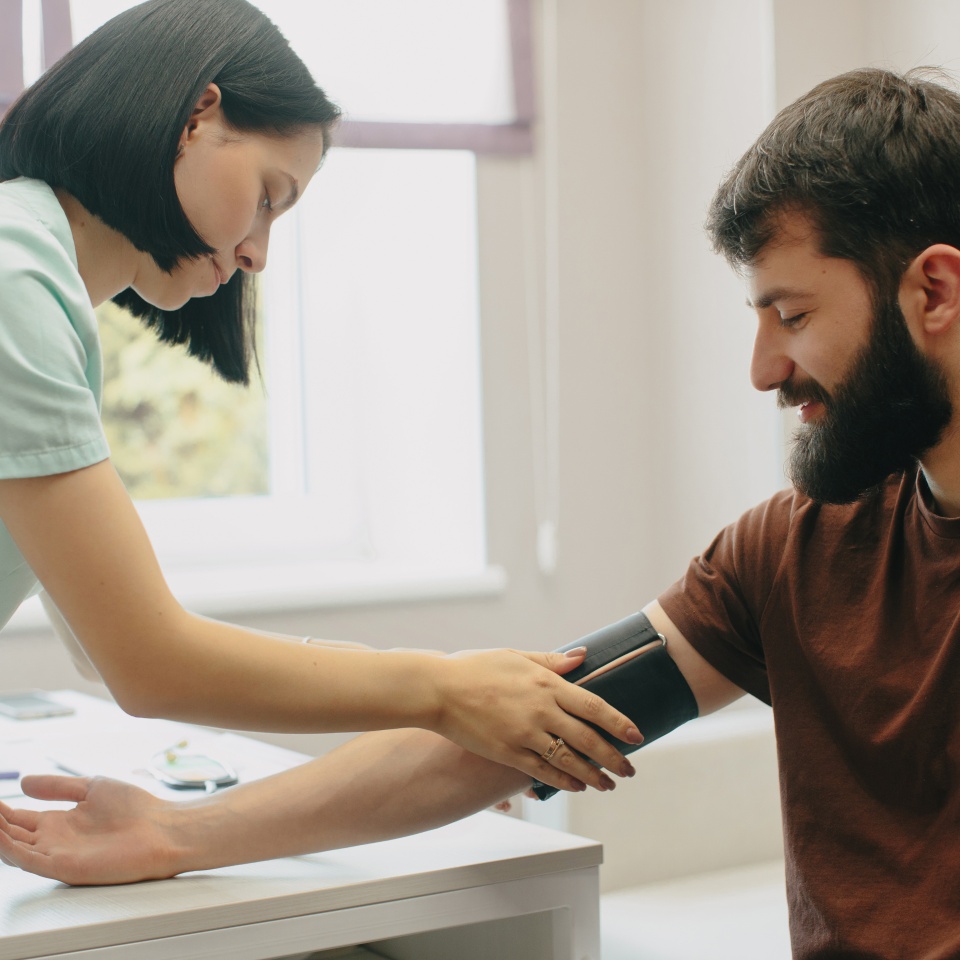 Healthcare professional checking a male patient's blood pressure at a clinic, focusing on medical examination and prevention