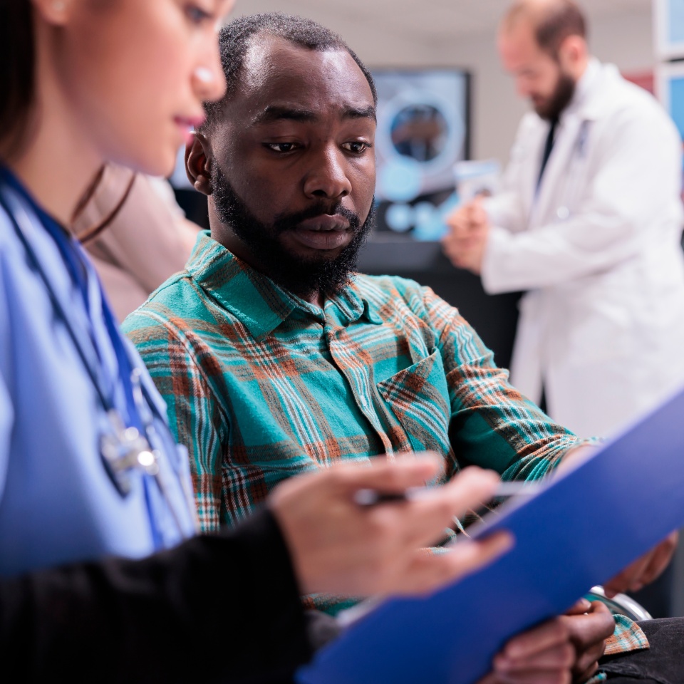 Close up of african american man reviewing medical records along with asian female member of in house hospital staff. Doctor indicating treatment to young male patient at sanatorium lobby.